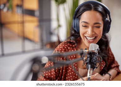 Cheerful young woman recording podcast in studio with copy space. Confident latin woman with headphones and microphone recording a podcast at home. Happy mexican girl talking on web radio.