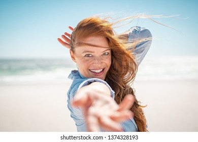 Cheerful young woman with red hair enjoying holiday at beach. Beautiful mature woman at sea during a windy day. Attractive girl smiling and looking at camera while feeling free at beach.