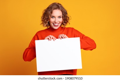 Cheerful young woman smiling for camera and holding at empty banner against yellow background