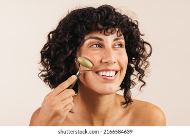 Cheerful Young Woman Smiling Happily While Massaging Her Face With A Jade Roller. Body Conscious Young Woman Taking Care Of Her Skin Using A Cosmetic Beauty Stone.