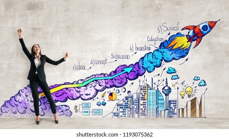 Cheerful Young Woman Standing On Concrete Wall Background With Business Sketch And Launching Rocker. Startup And Entrepreneurship Concept 