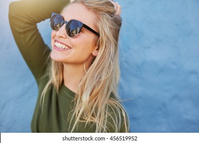 Cheerful young woman in sunglasses against blue background. Beautiful female model with long hair.