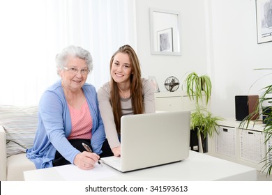 Cheerful Young Woman Teaching Computer To An Old Senior Woman At Home