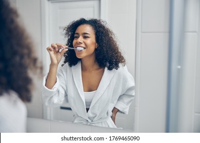 Cheerful young woman with a toothbrush in her hand looking at herself in the mirror - Powered by Shutterstock