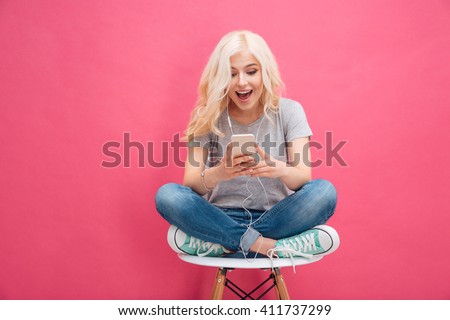Cheerful young woman using smartphone with headphones over pink background