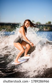 cheerful young woman wakesurfer with brown hair actively balancing on surfboard along the river wave