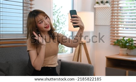 Cheerful young woman waving hand, chatting online, making video call on her smart phone