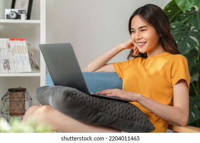 Cheerful Young Woman Wear Orange Shirt With Sitting On Sofa And Using Laptop Computer At Home.