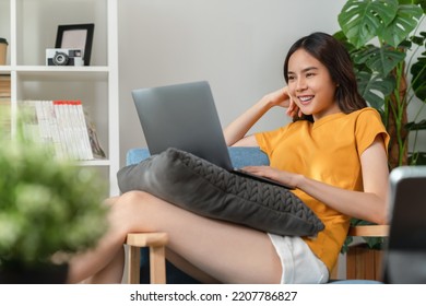 Cheerful Young Woman Wear Orange Shirt With Sitting On Sofa And Using Laptop Computer At Home.