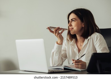 Cheerful Young Woman Working At Office, Female Employee Using Smartphone Voice Message While Sitting By Laptop At Workplace