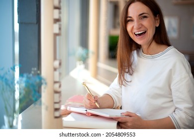 Cheerful young woman writing and keeping her personal a daily diary books. Concept of keeping a journal. Making list of future goals. Eating plans and appointments. Scheduling healthy meal plan. - Shutterstock ID 2054809553