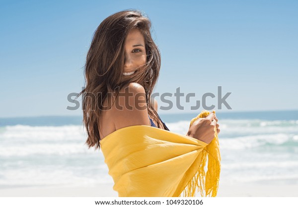 ビーチの黄色いサロンに着いた元気な若い女性 ビーチを楽しみ カメラを見ながら幸せな笑顔の女の子 夏休み中に黄色いスカーフを着て爽快に感じるラテン色の女性 の写真素材 今すぐ編集