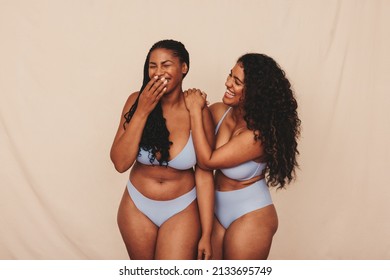 Cheerful Young Women Laughing In Blue Underwear. Two Happy Young Women Celebrating Their Natural Bodies And Curves In A Studio. Body Positive Young Women Standing Together Against A Studio Background.