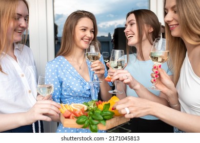 Cheerful young women standing together on terrace, drinking wine and eating snacks from plate closeup. Having fun and enjoying outdoor recreation. Girls party, hen night, female friendship, summer.