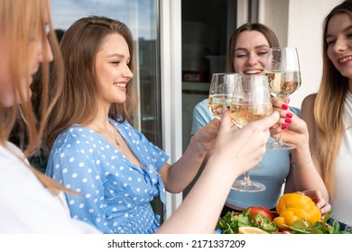 Cheerful young women standing together on terrace, clinking glasses and drinking wine closeup. Having fun and enjoying outdoor recreation. Girls party, hen night, female friendship, summer.