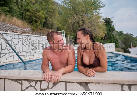 Cheerful youthful guy and lady resting while swimming pool outdoor. Couple in water.