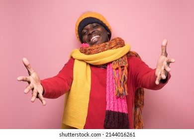 Cheerfull African Man Dressed In Several Hats And Scarfs Pulling Hands Towards Camera, Wanting To Cuddle, Smiling Broadly, Welcoming Friend To Come Into His Arms