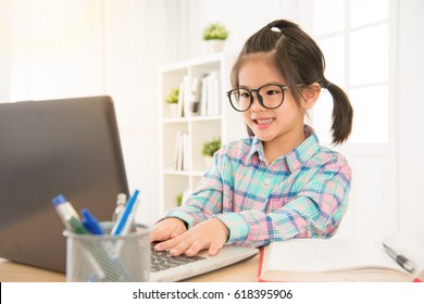 Cheerfully Cute Girl Children Excited Using Computer Learning Schoolwork. Asian Glasses Colorful Shirt Kid Enjoy E-learning In Holiday At Home.