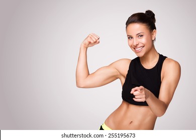 Cheerfully smiling mixed race sporty woman demonstrating biceps, isolated on white background