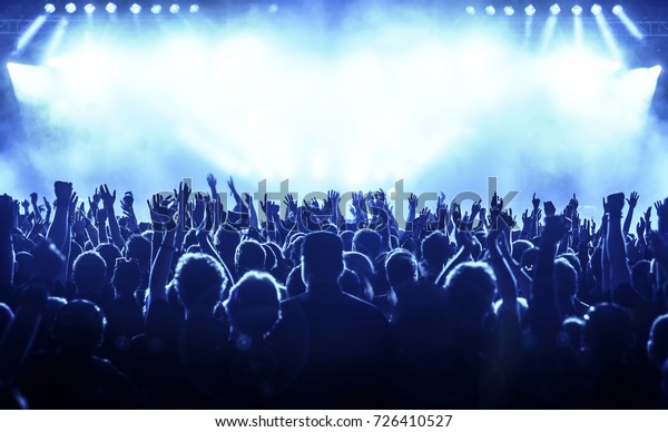 cheering\
crowd at rock concert in front of bright\
lights