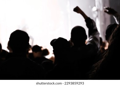 Cheering crowd and stage lights with space for your text. Defocus silhouette of people raise hand up in music concert with black and yellow color spotlight on stage background. Out of focus.