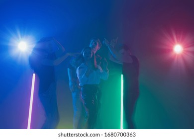 Cheering dance party, performance concept. Crowd shadow of people dancing with neon colorful lights raised hands up on dark background. Celebration, holiday, weekend, nightlife and positive vibes.