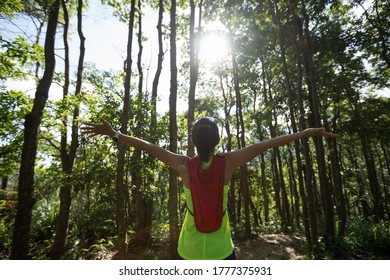Cheering ftness woman trail runner outstretched arms to sunshine  when running in tropical forest
