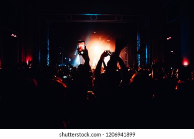 Cheering Stage Crowd Raises Hands In Front Of The Stage. Red Light Screen Behind The Stage. 