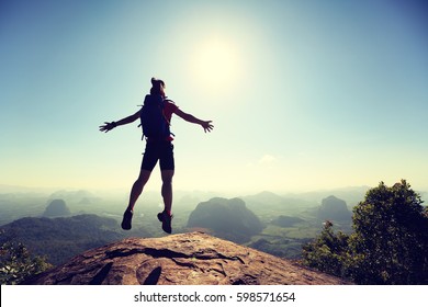 Cheering Successful Young Woman Hiker Jumping On Mountain Top Cliff Edge