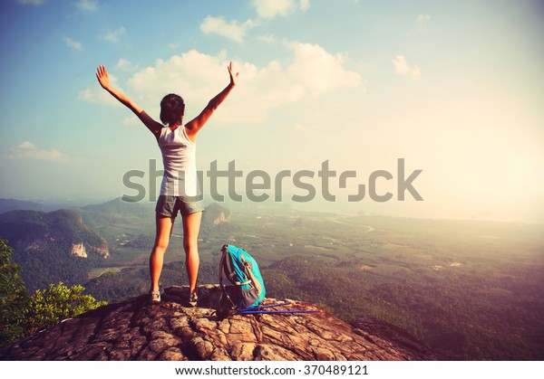 cheering woman hiker open arms at mountain peak