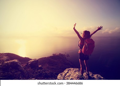 cheering young woman backpacker at sunrise seaside mountain peak - Powered by Shutterstock