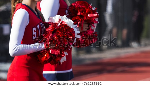 Cheerleaders pom poms glistening in the sun during\
a high school football\
game.
