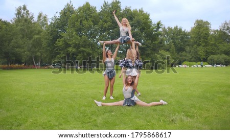 Cheerleaders practicing athletic elements preparing for performance. Team of sporty cheerleading girls in grey and white uniform training outdoors