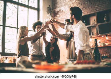 Cheers To Best Friends! Low Angle Of Cheerful Young People Cheering With Champagne Flutes And Looking Happy While Having Party On The Kitchen 