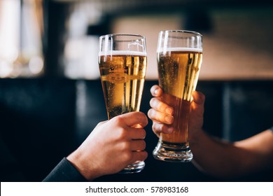 Cheers. Close-up of two men in shirts toasting with beer at the bar counter