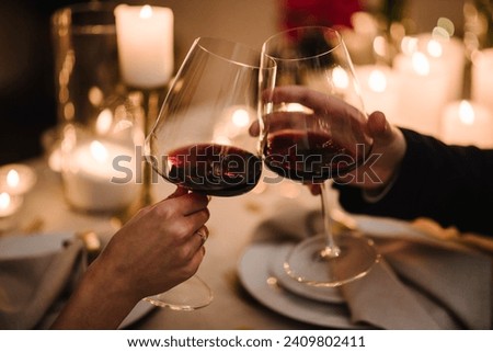 Cheers. Couple in love drinking wine. Romantic date by candlelight at night. Hands man and woman hold glasses at home. Toast. Dinner setup table for couple on Valentine's day. Proposal hand and heart.