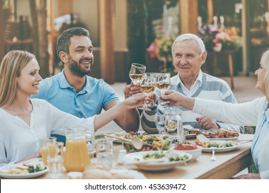 Cheers to family! Happy young and senior couples sitting at the dining table and toasting with wine - Powered by Shutterstock