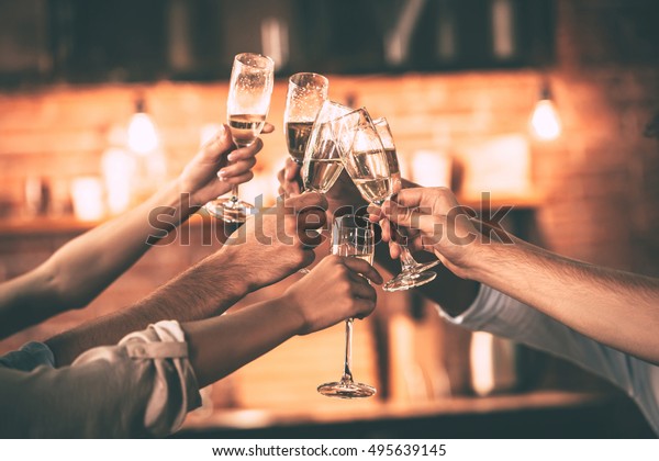Cheers! Group of people cheering with\
champagne flutes with home interior in the\
background