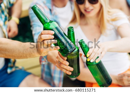 Cheers! Group of young people men and woman holding and toasting with green bottles of beer on river background. Celebrating oktoberfest with friends outdoor. Barbecue, hanging out, relaxing concepts.