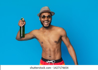 Cheers, Man. Friendly Black Guy In Swimwear Greeting With Beer Bottle, Blue Studio Background