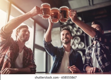 Cheers, my friends! Three handsome men are drinking beer, celebrating meeting and smiling.