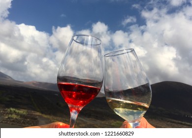 Cheers With Red And White Wine Shining Glasses In Middle Of Volcanic Vineyards In La Geria During Beautiful Day On Spanish Island Lanzarote