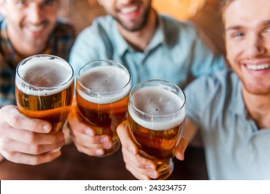 Cheers To Success! Top View Of Three Happy Young Men In Casual Wear Toasting With Beer While Sitting In Bar Together