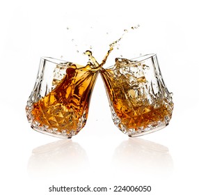 Cheers. Whiskey Toast. Two Glasses Clicking Together Over White Background. Splashing Whiskey On Glasses Of Cut Glass