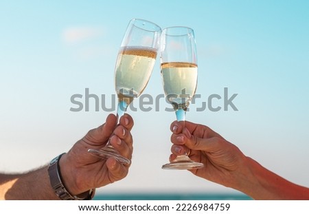 Cheers with wine glasses in a beautiful background sunset beach. couple hold champagne and celebrate holidays. hands of man with watch. 