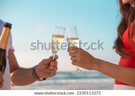 Cheers with wine glasses in beautiful background sunset beach. Couple hold champagne and celebrate holidays. Hands of man with watch and girl in red t-shirt.