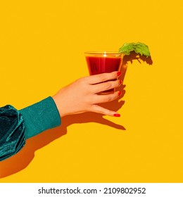 Cheers. Woman's Hand With Bloody Mary Glass Isolated On Bright Yellow Neon Background Concept Of Taste, Alcoholic Drinks. Complementary Colors, Blue, Yellow And Green. Pop Art. Copy Space For Ad, Text