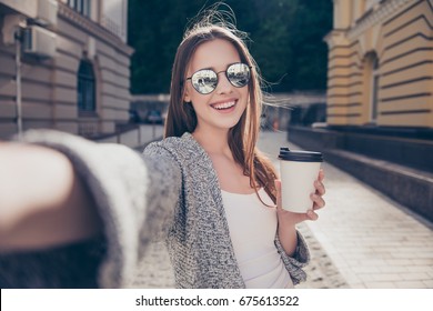 Cheert! Selfie time! Young happy lady in a spring vacation, walking in the city, drinking coffee, photographing herself on a sunny day - Powered by Shutterstock