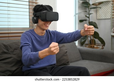 Cheery Asian man in VR headset holding imaginary steering wheel of virtual car, playing a driving simulation video game - Shutterstock ID 2253852829
