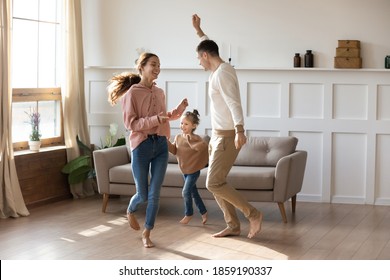 Cheery couple dancing with little daughter barefoot on wooden laminate floor with underfloor heating system in modern warm living room. New home, bank loan and lending, hobby and fun with kids concept - Shutterstock ID 1859190337